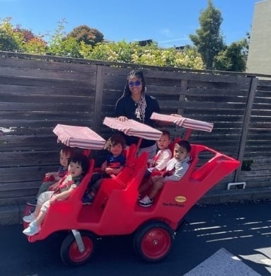Kids Konnect Downtown teacher taking toddlers for a ride in red stroller wagon during outdoor time