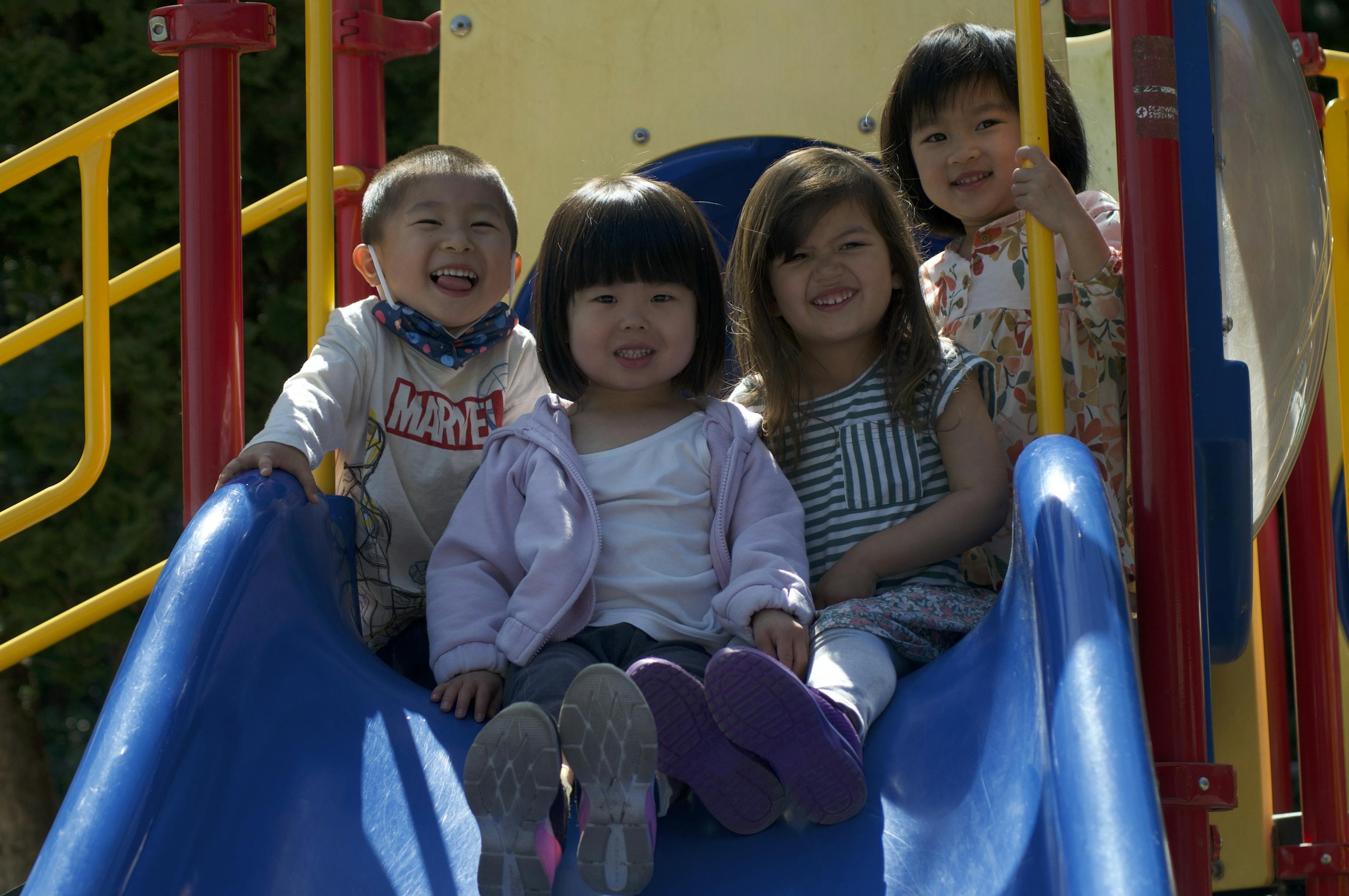 Smiling preschoolers sitting together on a blue slide at Kids Konnect outdoor playground