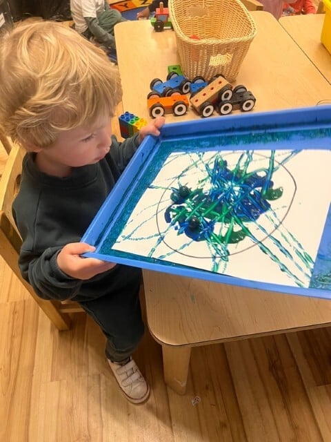 Preschool child displaying marble rolling art as part of a creative STEAM project at Kids Konnect