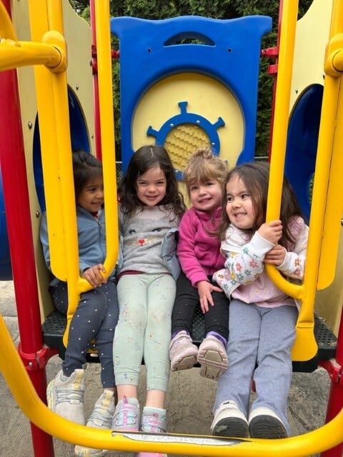 Four preschoolers laughing together on slide at Kids Konnect playground in San Mateo