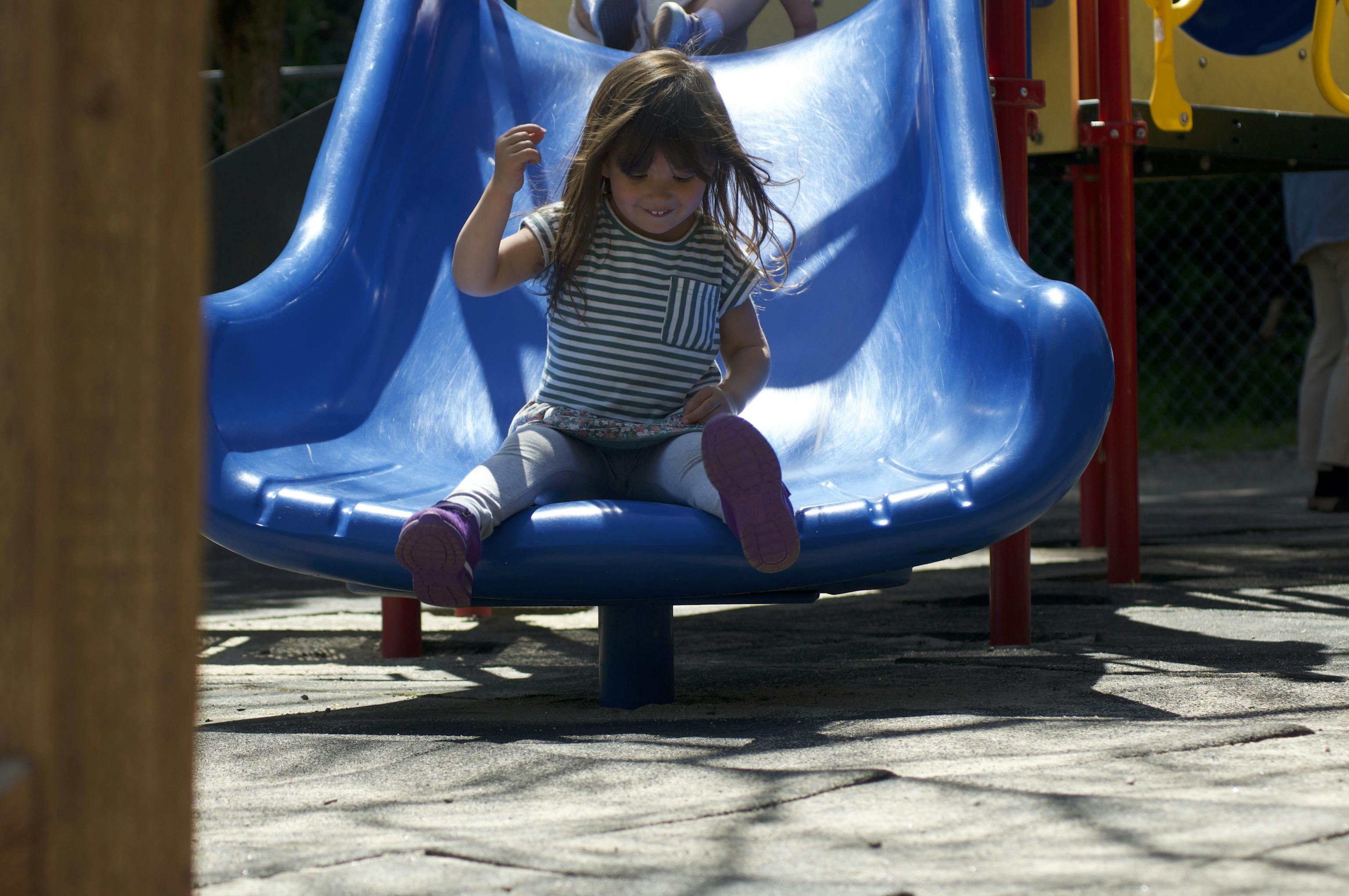 Preschool girl sliding down blue outdoor play structure at Kids Konnect San Mateo Bunker Hill