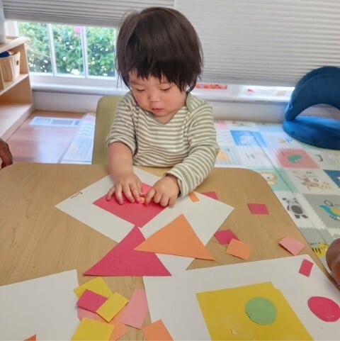 Toddler developing fine motor skills while gluing colorful paper shapes at Kids Konnect