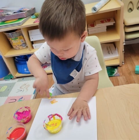 Toddler focused on finger painting during creative art time at Kids Konnect